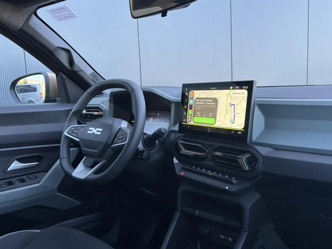 Vue intérieure côté conducteur du Dacia Duster 2026 gris, avec écran tactile central et volant multifonctions.