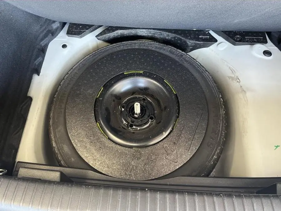 Roue de secours noire dans le coffre blanc du DS3 Crossback 2022 vue en plongée, sans autres éléments visibles.