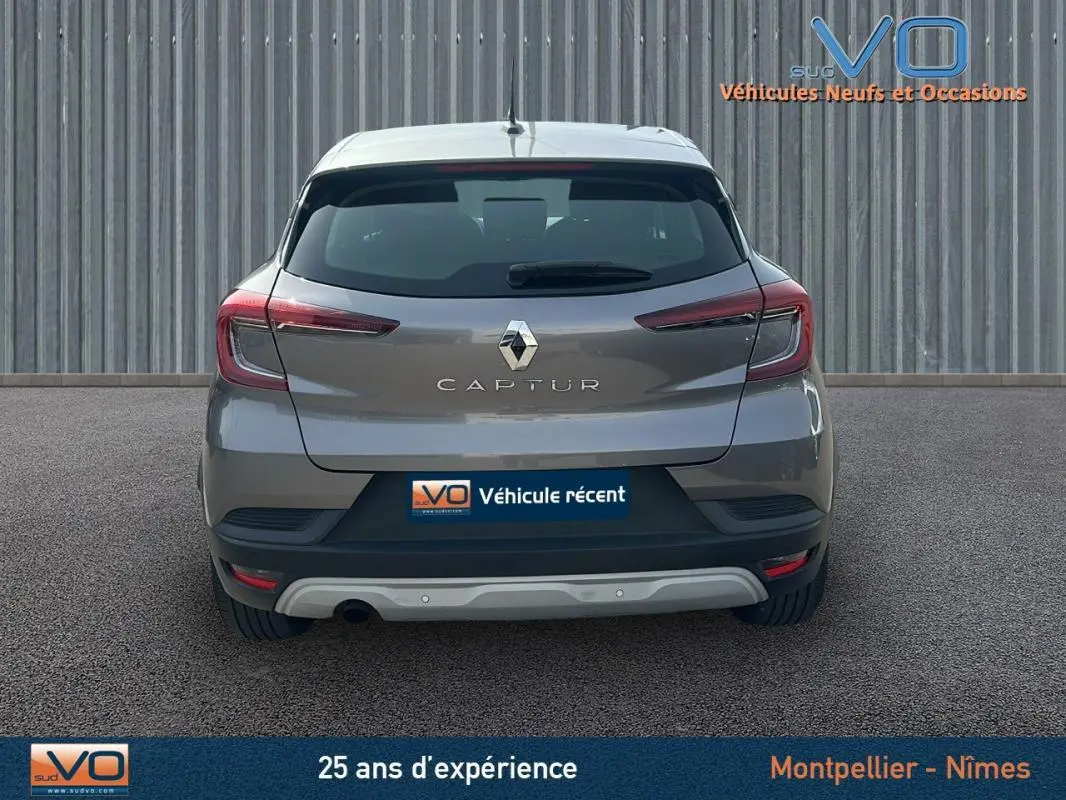 Vue arrière d'un Renault Captur gris 2020 avec feux arrière allumés sur fond urbain neutre.