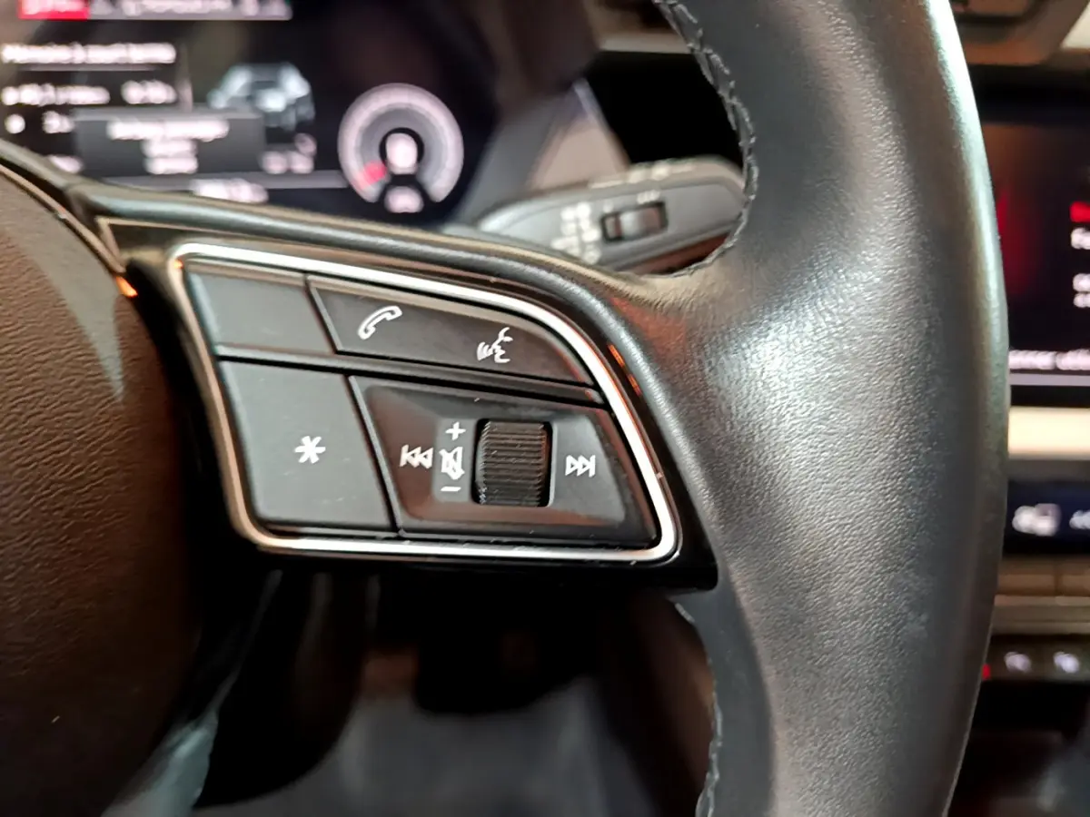 Gros plan sur les commandes gauche du volant cuir noir de l'Audi A3 35 TFSI 2023 avec affichage numérique flou en arrière-plan.