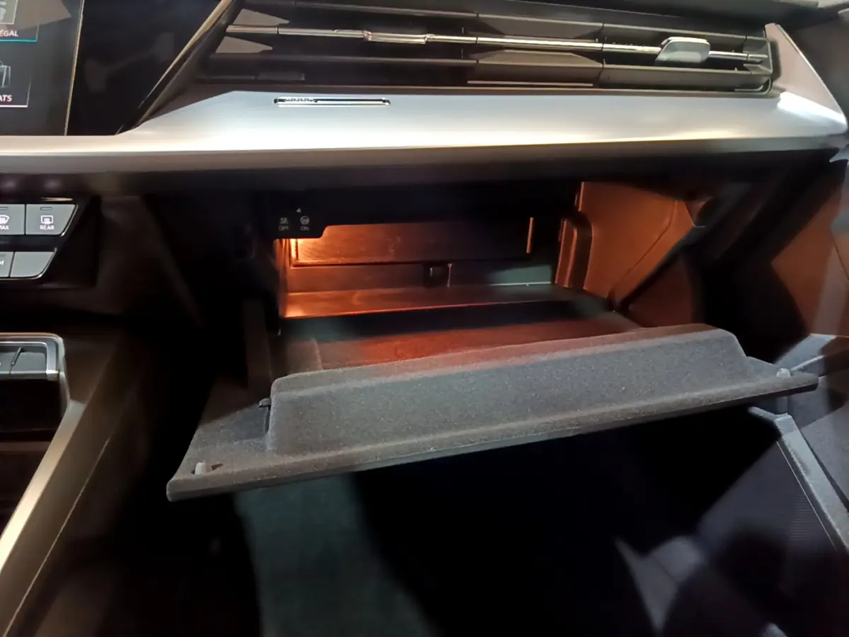 Vue rapprochée de la boîte à gants ouverte de l'Audi A3 35 TFSI Business Line, éclairage intérieur visible.