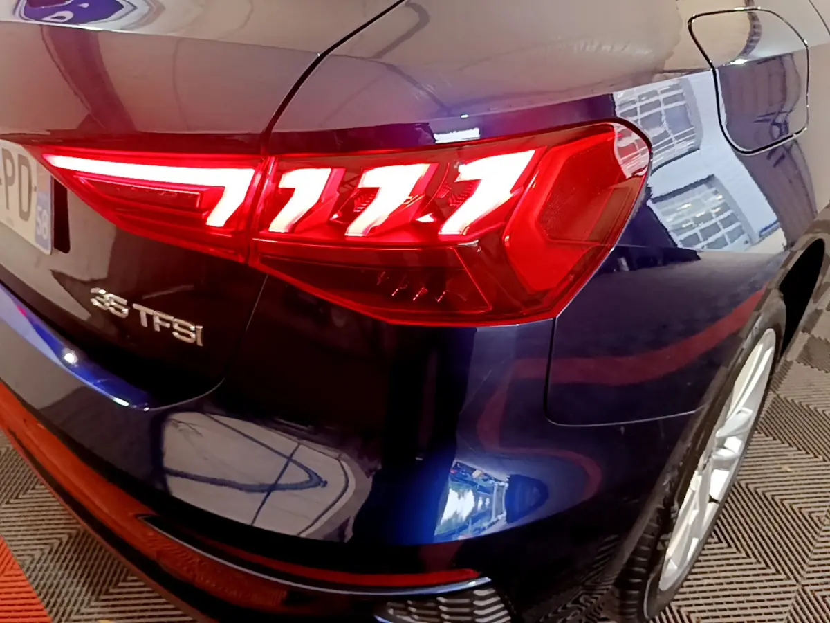 Gros plan sur le feu arrière droit rouge vif d'une Audi A3 35 TFSI bleu foncé, avec logo et jante visible.