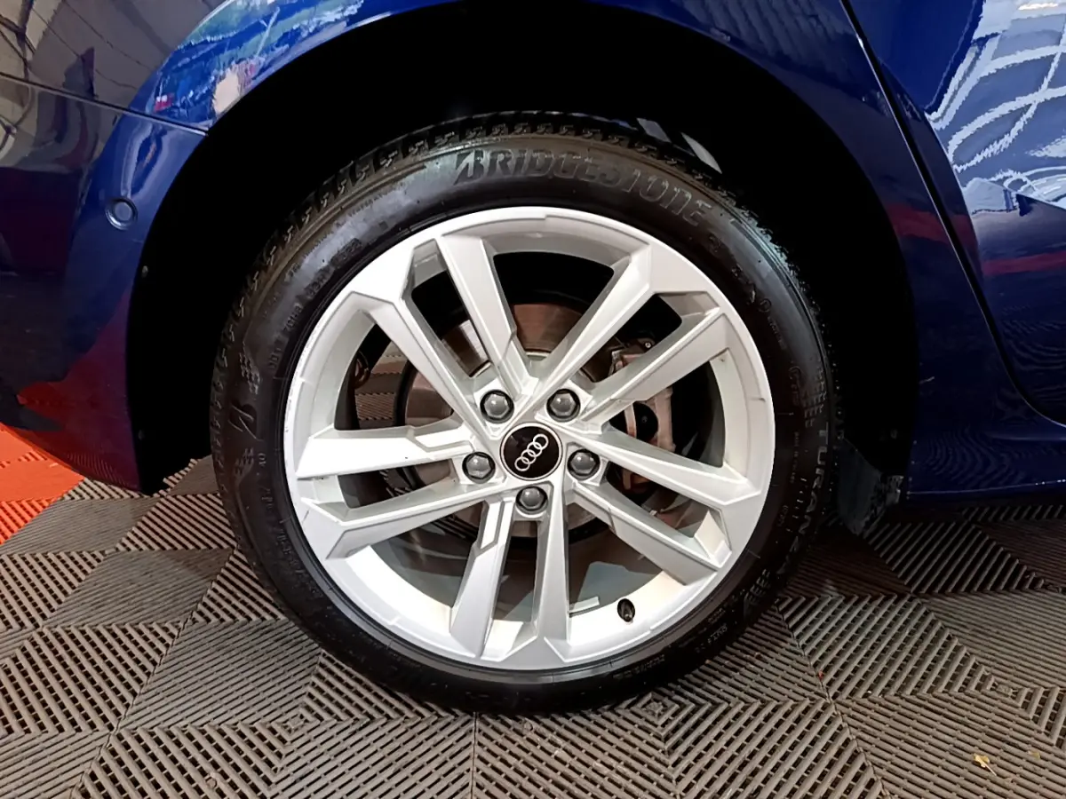 Gros plan sur la roue avant gauche d’une Audi A3 bleu 2023 avec jante alliage argentée et logo Audi central.