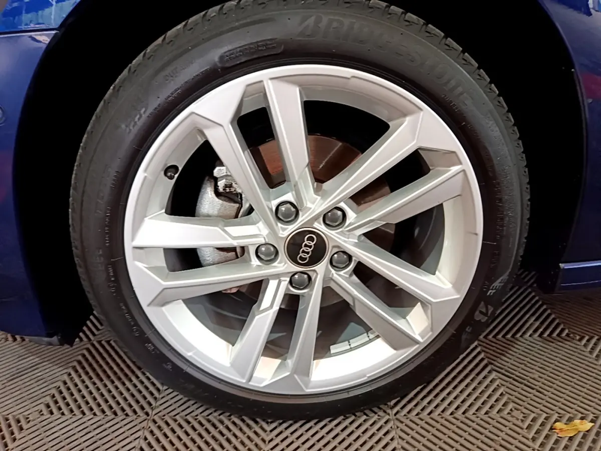 Gros plan sur la jante argentée d'une Audi A3 bleu 2023, mettant en valeur le logo Audi au centre.