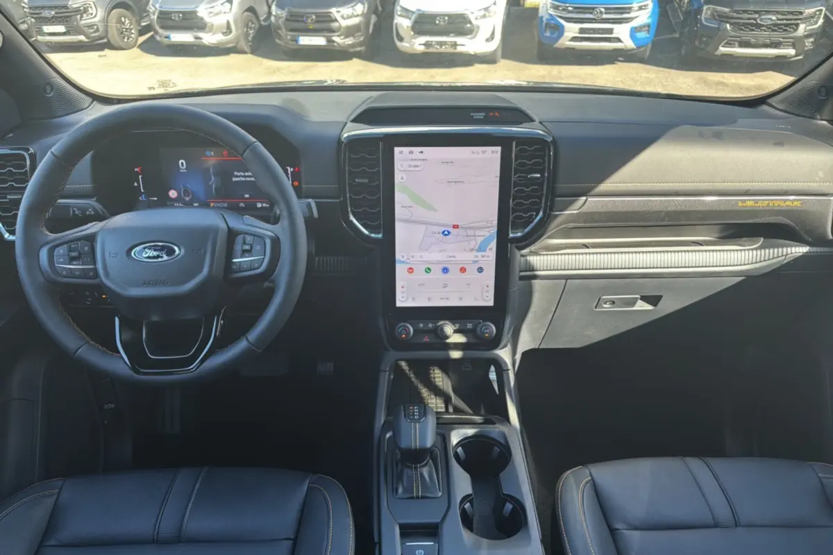 Vue intérieure frontale du Ford Ranger Wildtrak 2025 avec tableau de bord noir, écran tactile vertical et volant cuir multifonctions.