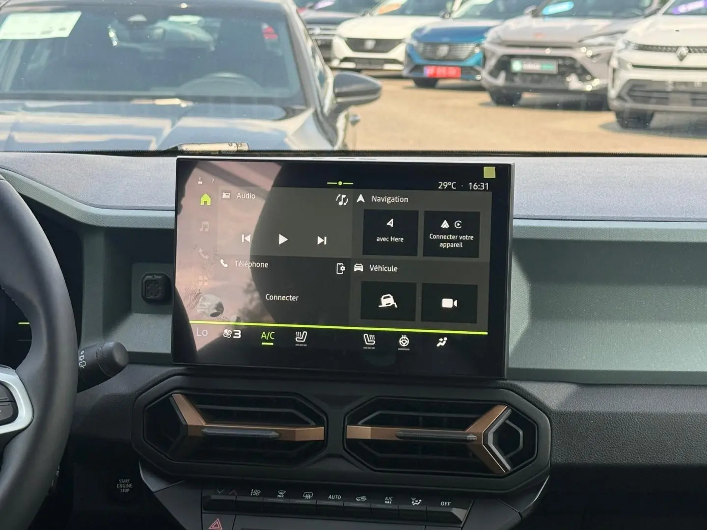 Vue intérieure centrée sur l'écran tactile du tableau de bord du Dacia Duster 2026, avec commandes clim et volant partiel visible.