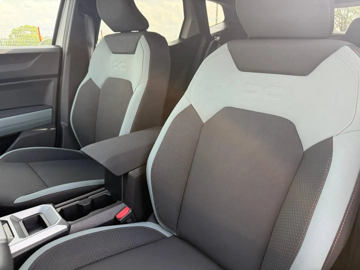 Vue rapprochée des sièges avant gris clair et noir du Dacia Duster 2026 avec accoudoir central et logo DC embossé.