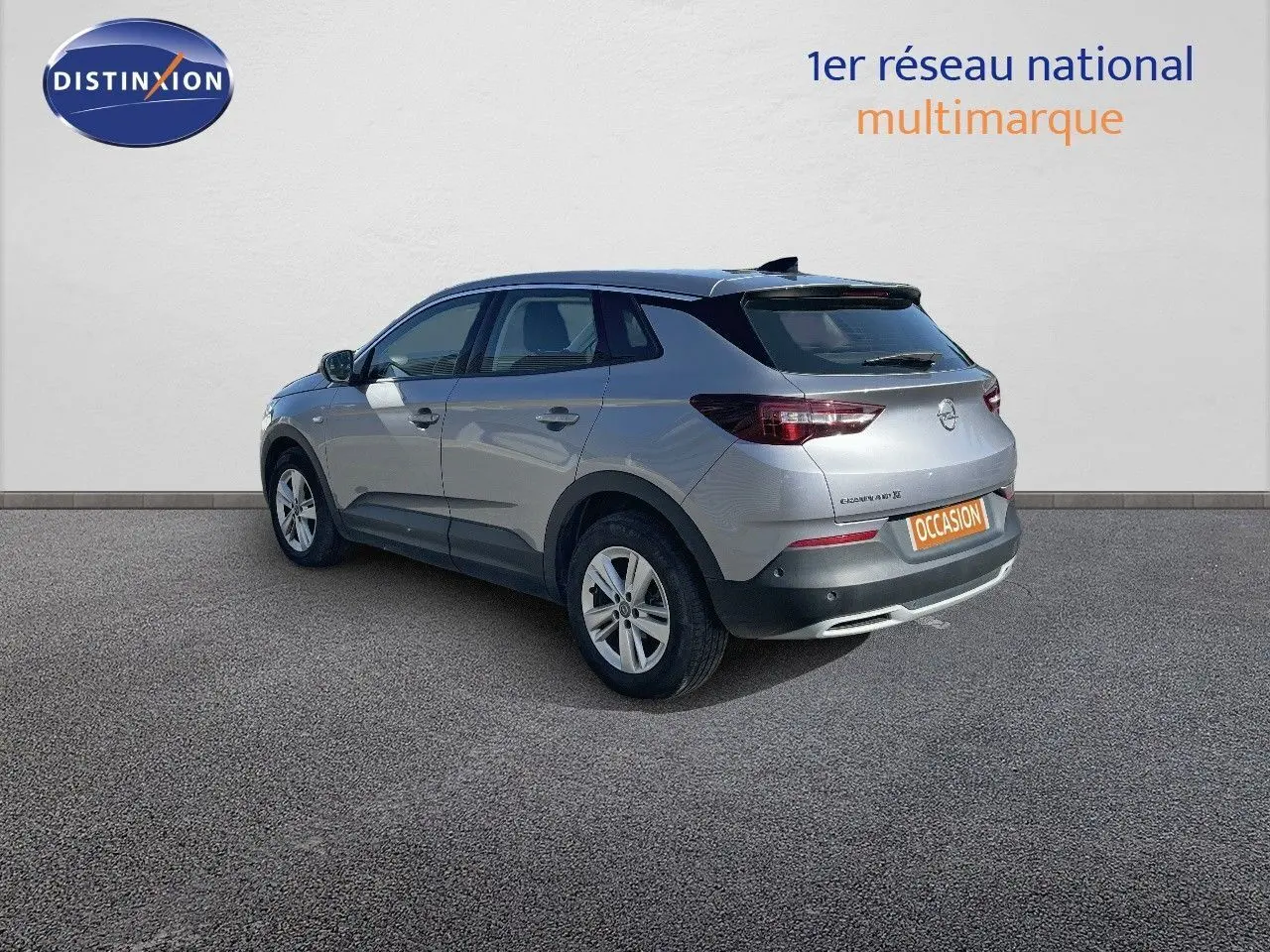 Opel Grandland X gris quartz métal vu en 3/4 arrière droit sur fond neutre avec plaque occasion visible.