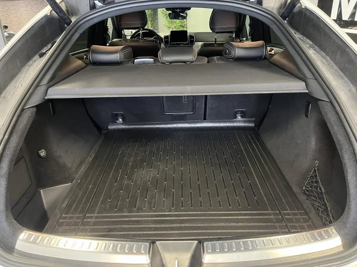 Coffre ouvert vu de l'arrière d'un Mercedes GLE Coupé blanc avec cache-bagages et tapis de protection noir.