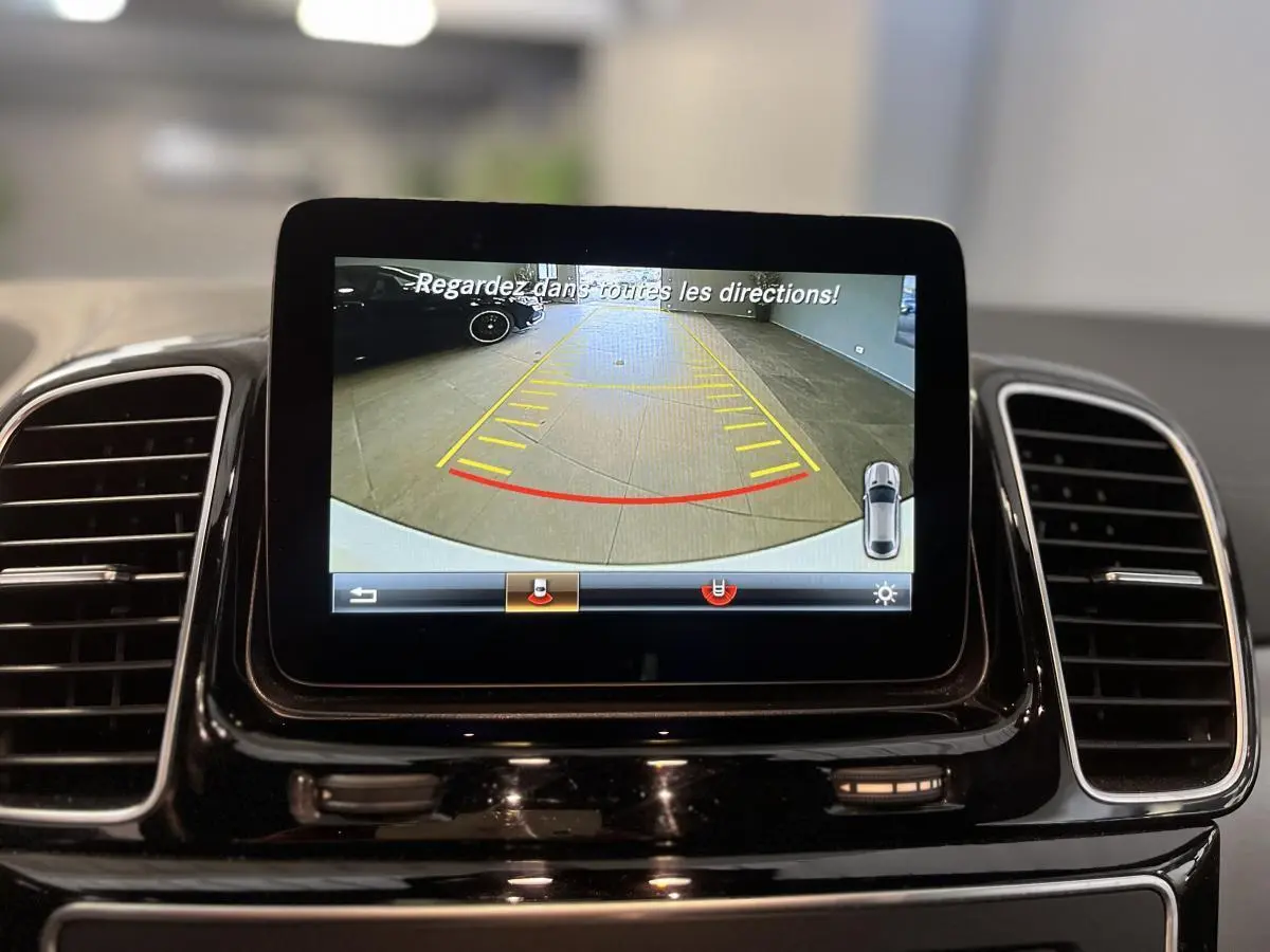 Écran central du Mercedes GLE Coupé blanc 2016 affichant la caméra de recul avec lignes de guidage en intérieur.