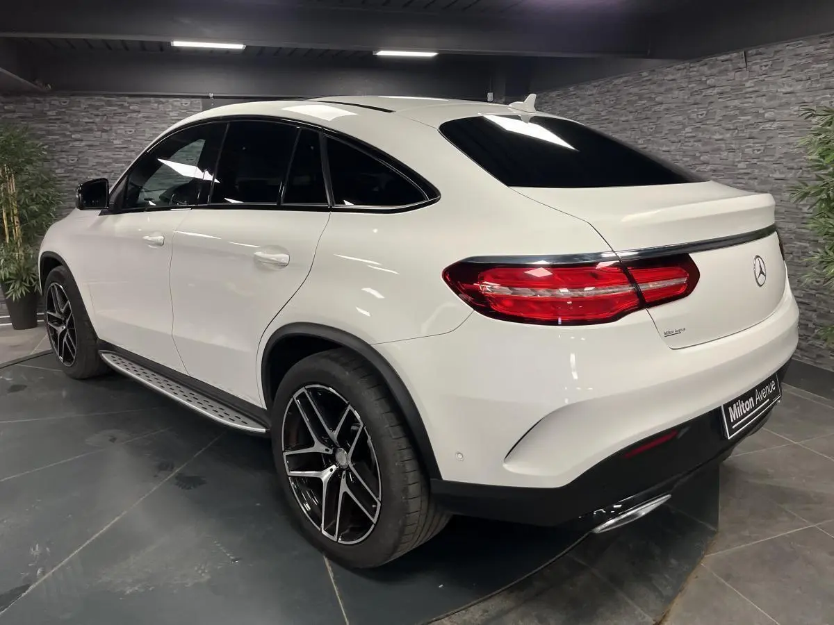 Vue 3/4 arrière droite d'un Mercedes GLE Coupé blanc avec jantes AMG noires et toit ouvrant panoramique.