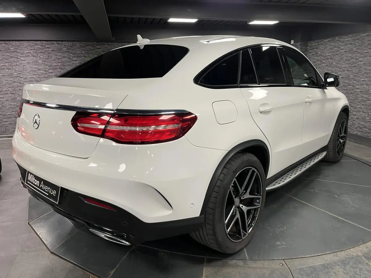 Vue 3/4 arrière droite d'un Mercedes GLE Coupé 350 d blanc avec jantes AMG noires et toit panoramique.