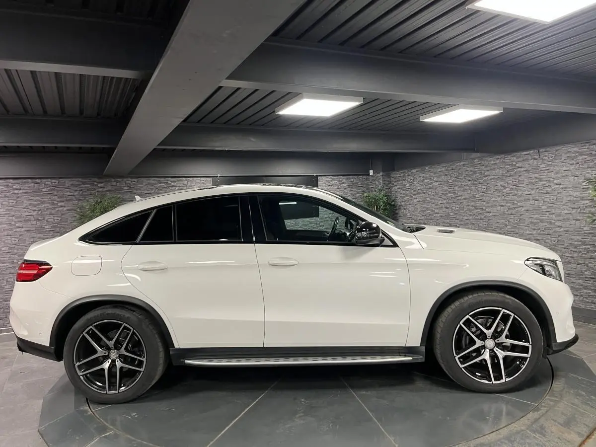 Profil côté gauche d'un Mercedes GLE Coupé 350 d blanc avec jantes AMG noires et vitres teintées dans un garage.