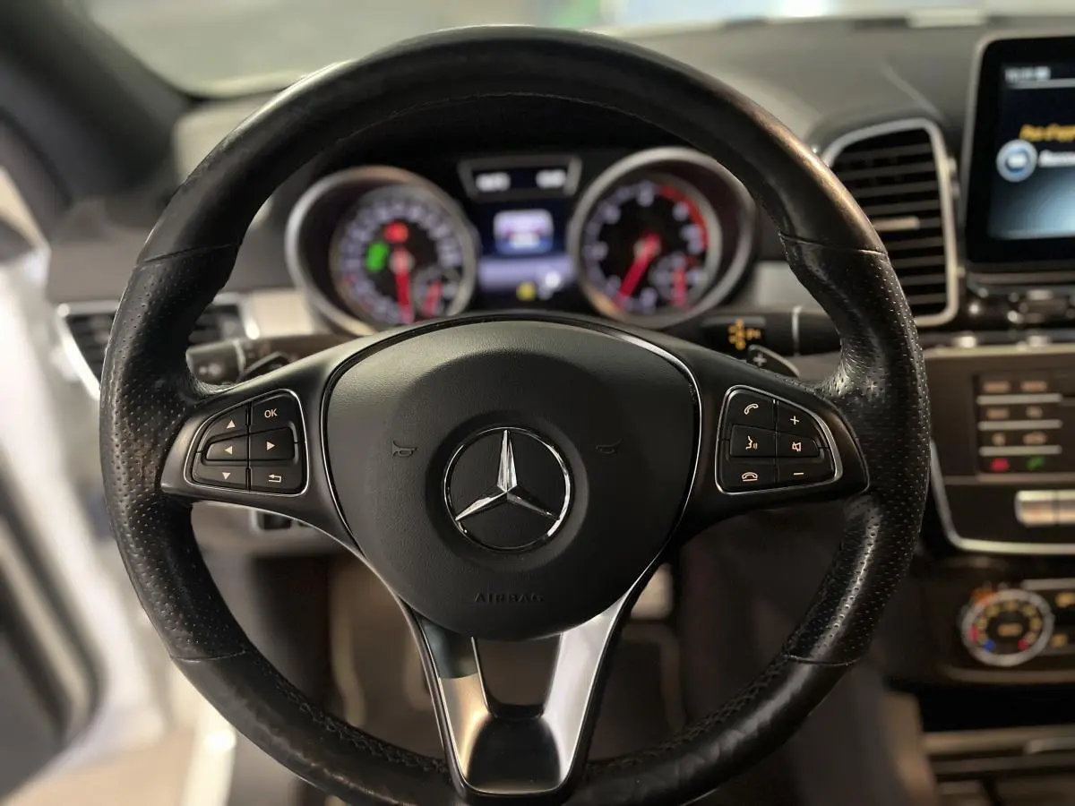 Volant en cuir noir multifonctions Mercedes avec logo étoile, tableau de bord et écran central flous en arrière-plan