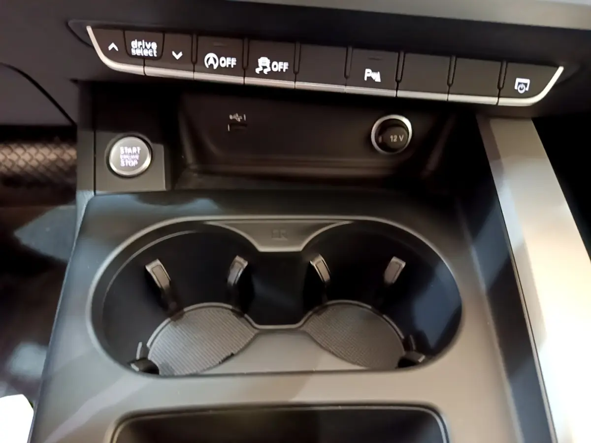 Gros plan sur la console centrale noire de l'Audi A5 35 TFSI avec boutons de commande et porte-gobelets.
