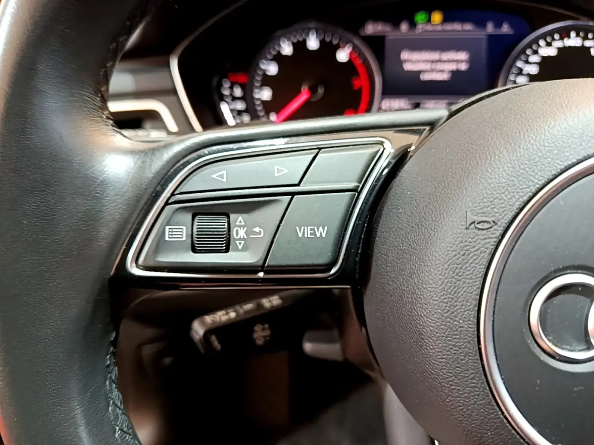 Gros plan sur le volant cuir noir de l'Audi A5 2021, côté gauche avec commandes multifonctions et tableau de bord en arrière-plan.