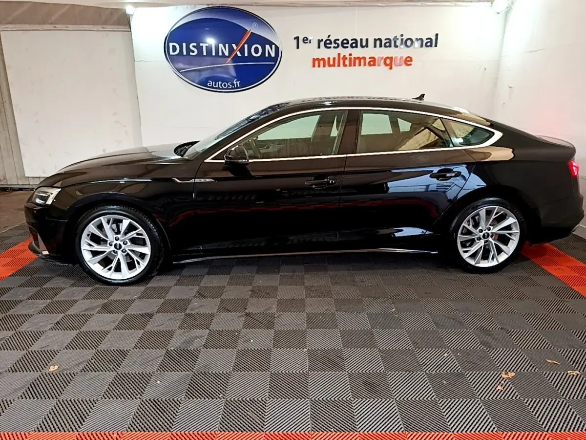 Profil côté gauche d'une Audi A5 noire 2021 stationnée en intérieur avec jantes argentées et toit panoramique.