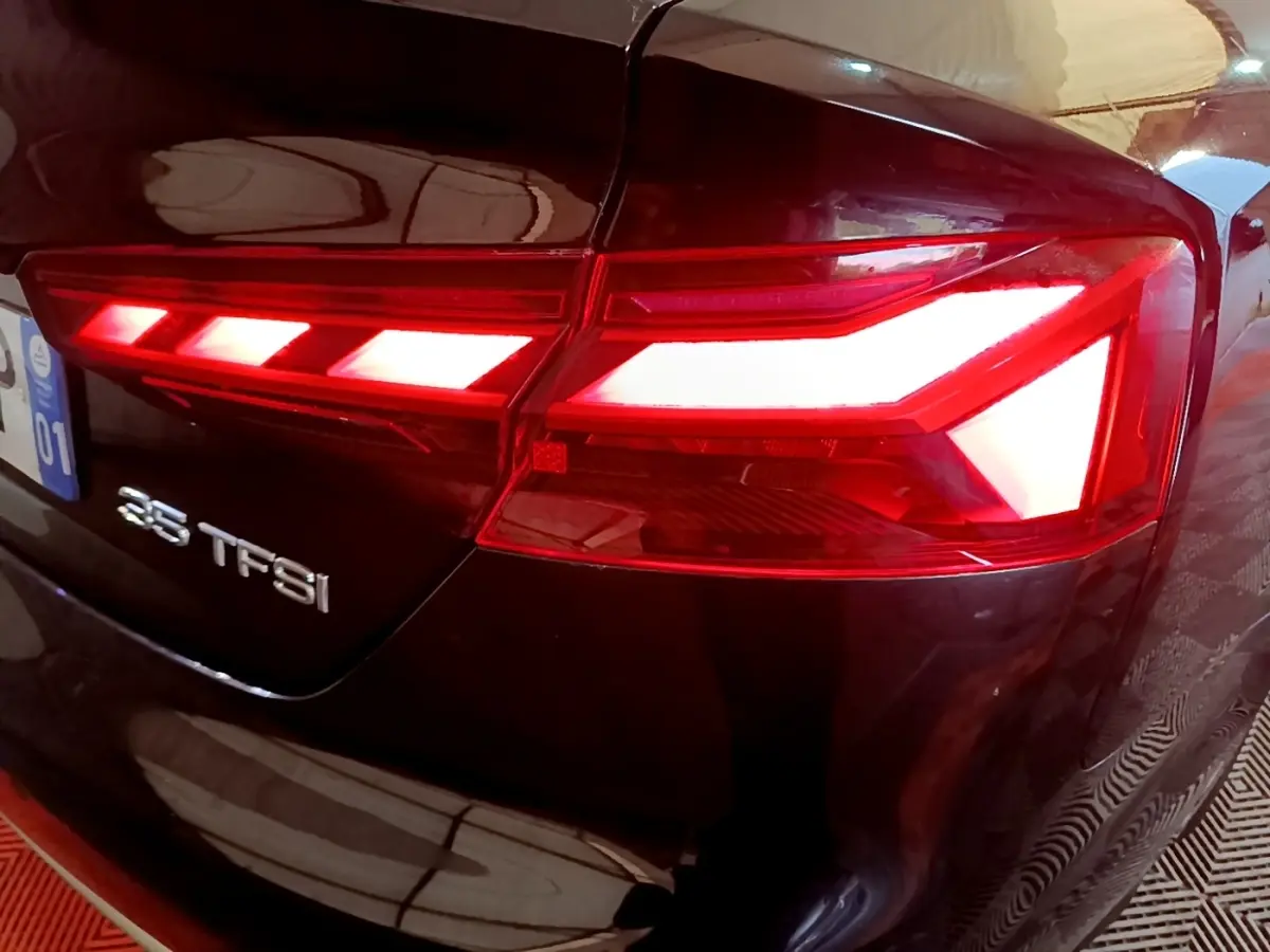 Feu arrière droit allumé d'une Audi A5 35 TFSI noire, vue rapprochée sur le logo et la carrosserie brillante.