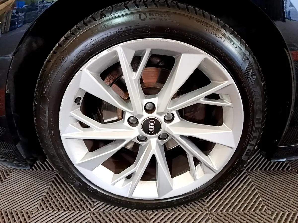 Gros plan sur la jante argentée d'une Audi A5 noire, mettant en valeur le logo Audi au centre du pneu Michelin.
