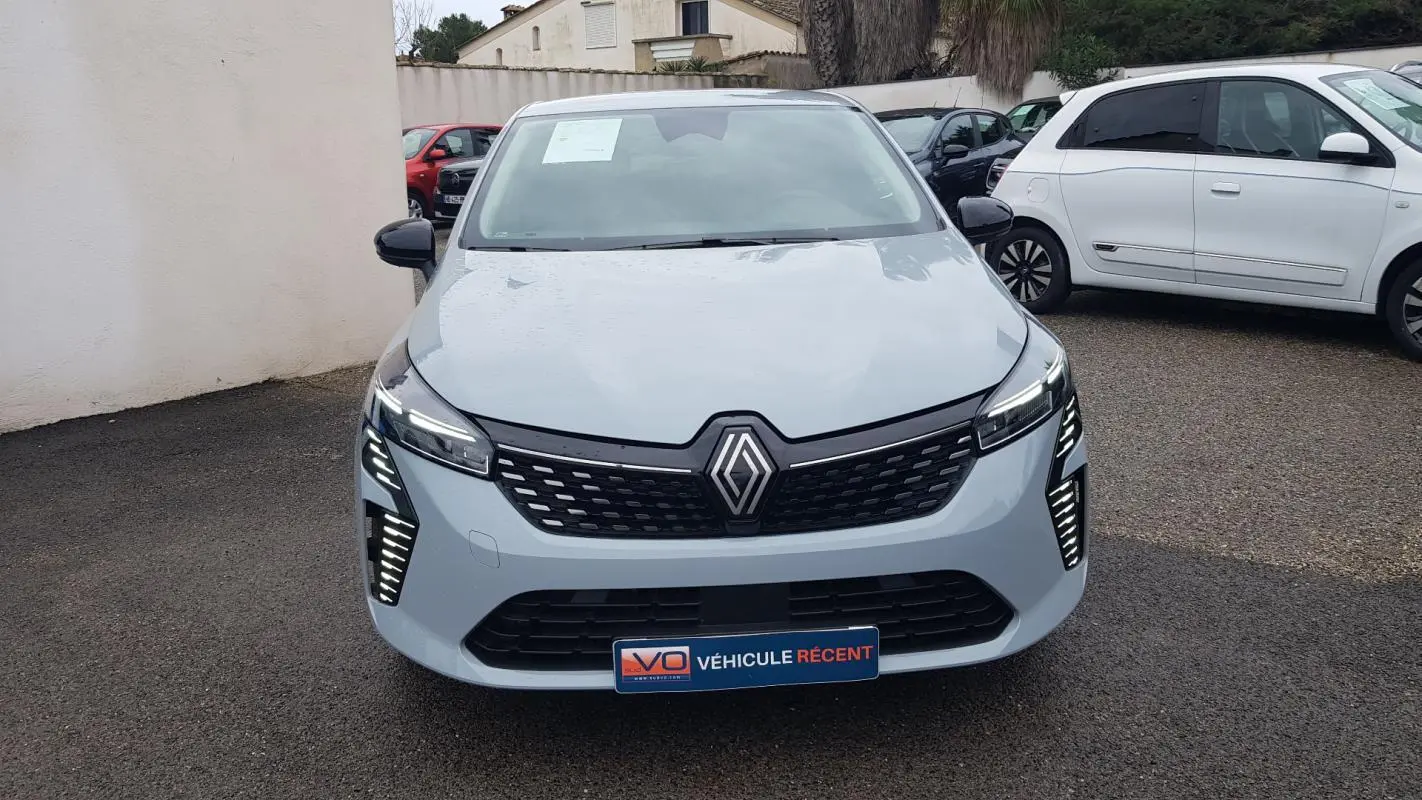 Vue frontale d'une Renault Clio gris clair 2025 avec feux LED allumés et calandre noire distinctive.