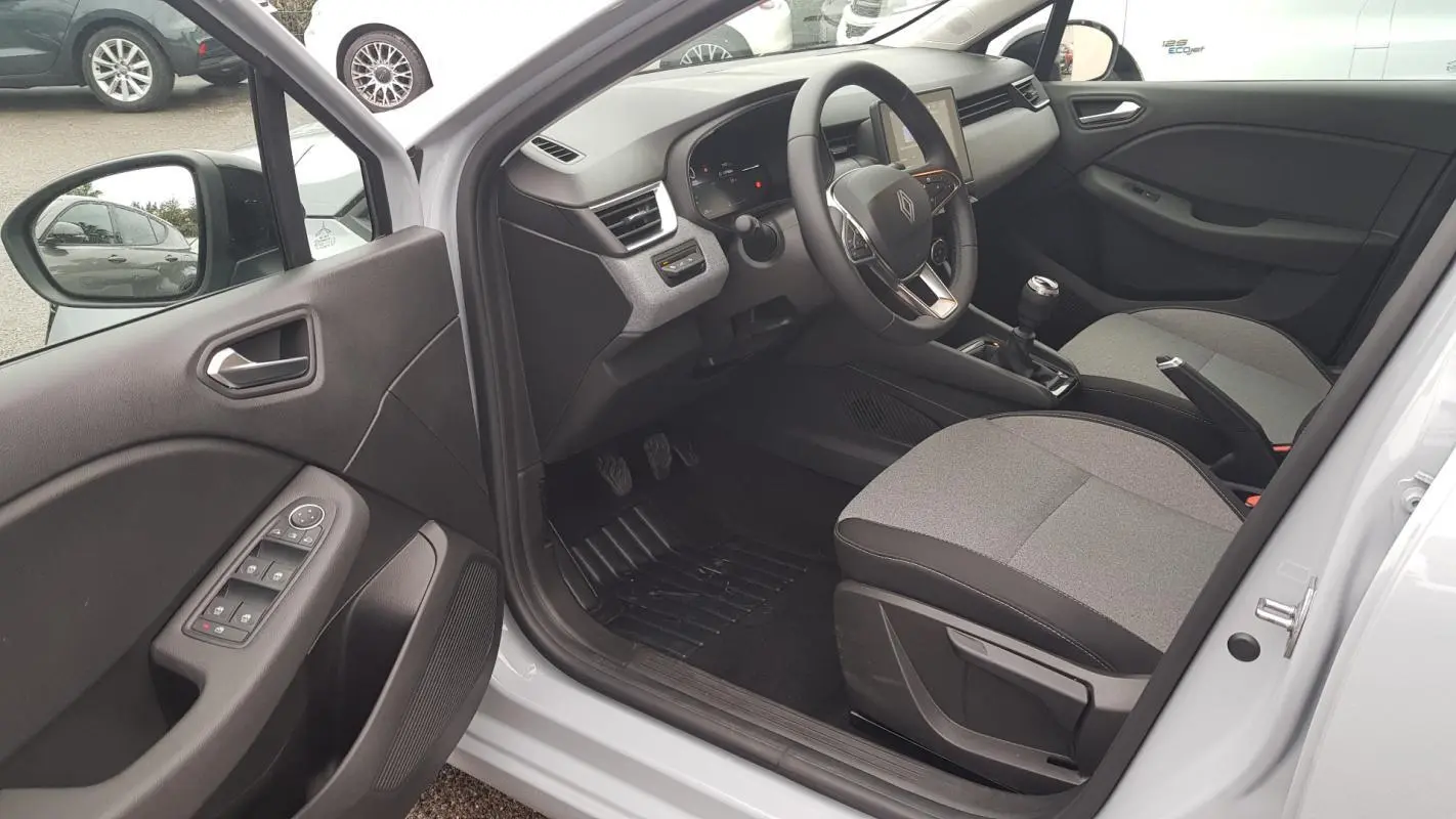 Vue intérieure côté conducteur de la Renault Clio gris 2025, montrant le tableau de bord et la boîte manuelle.