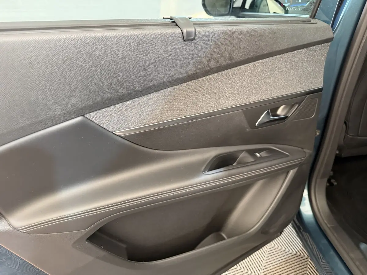 Vue intérieure du panneau de porte arrière droite du Peugeot 5008 bleu, avec poignée argentée et commandes de fenêtre.
