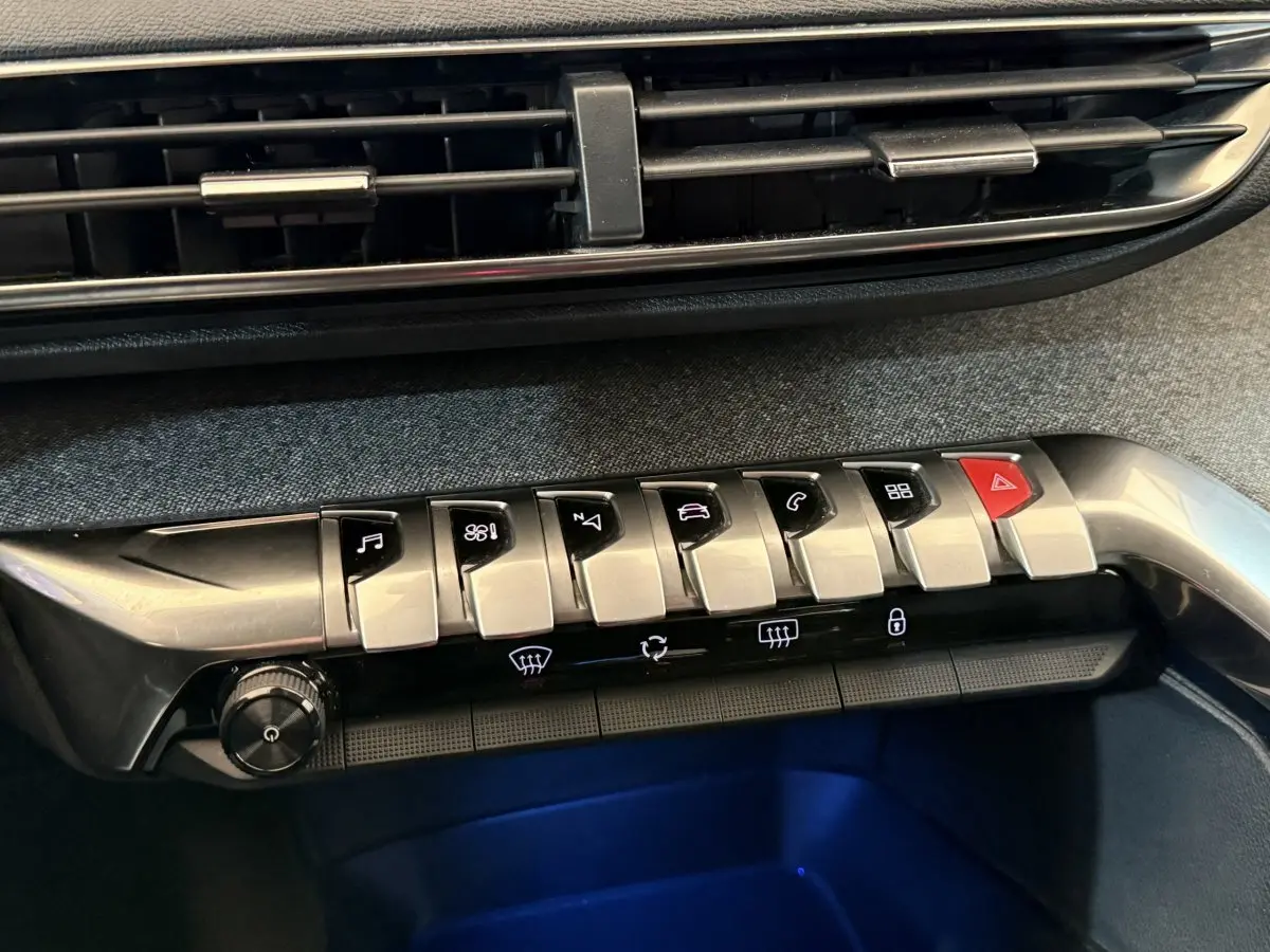 Gros plan sur la console centrale du Peugeot 5008 bleu, montrant les boutons de commande et la ventilation.