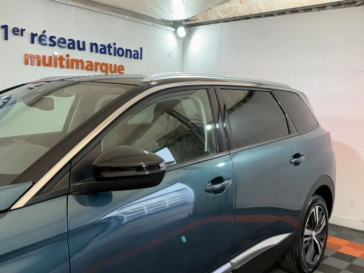 Vue latérale côté gauche d'un Peugeot 5008 bleu avec rétroviseur noir et vitres teintées dans un garage.