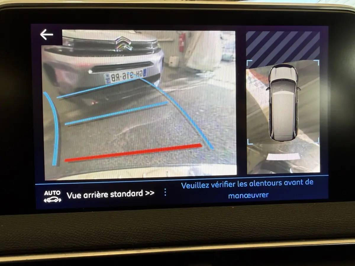 Écran de caméra de recul montrant une voiture grise vue de l’arrière avec lignes de guidage bleues et rouges.