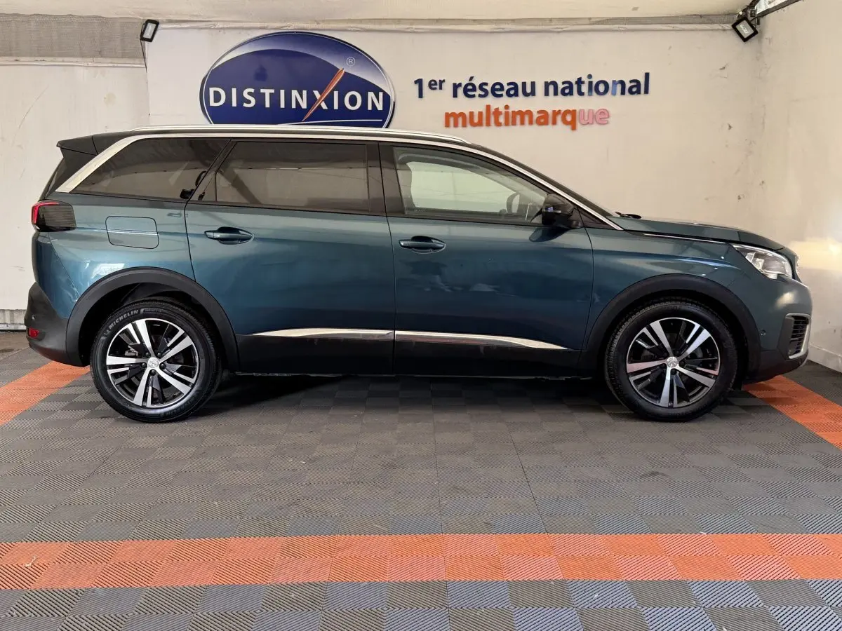 Profil droit d’un Peugeot 5008 bleu 2019 avec vitres teintées et jantes alliage bicolores, en intérieur showroom.