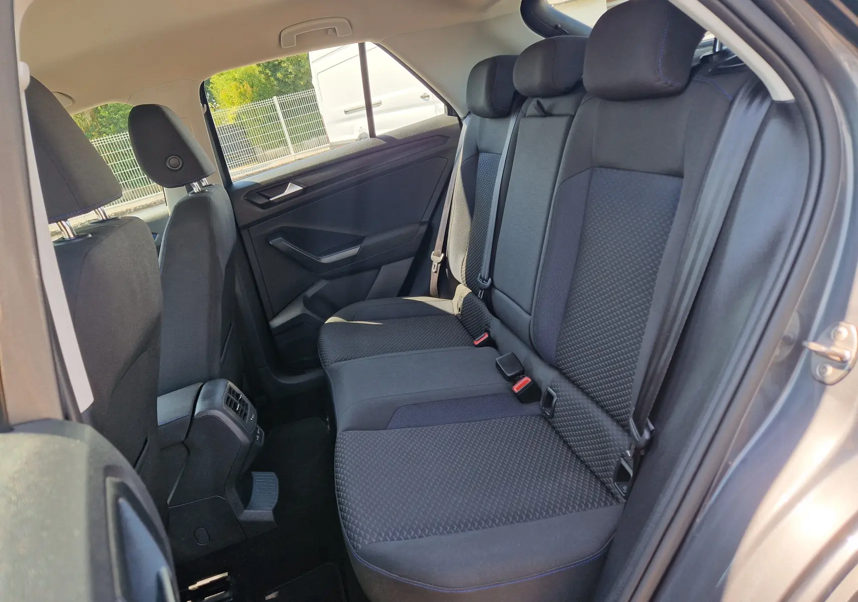 Vue intérieure côté droit des sièges arrière noirs du Volkswagen T-Roc gris foncé, montrant les appuie-têtes et ceintures.