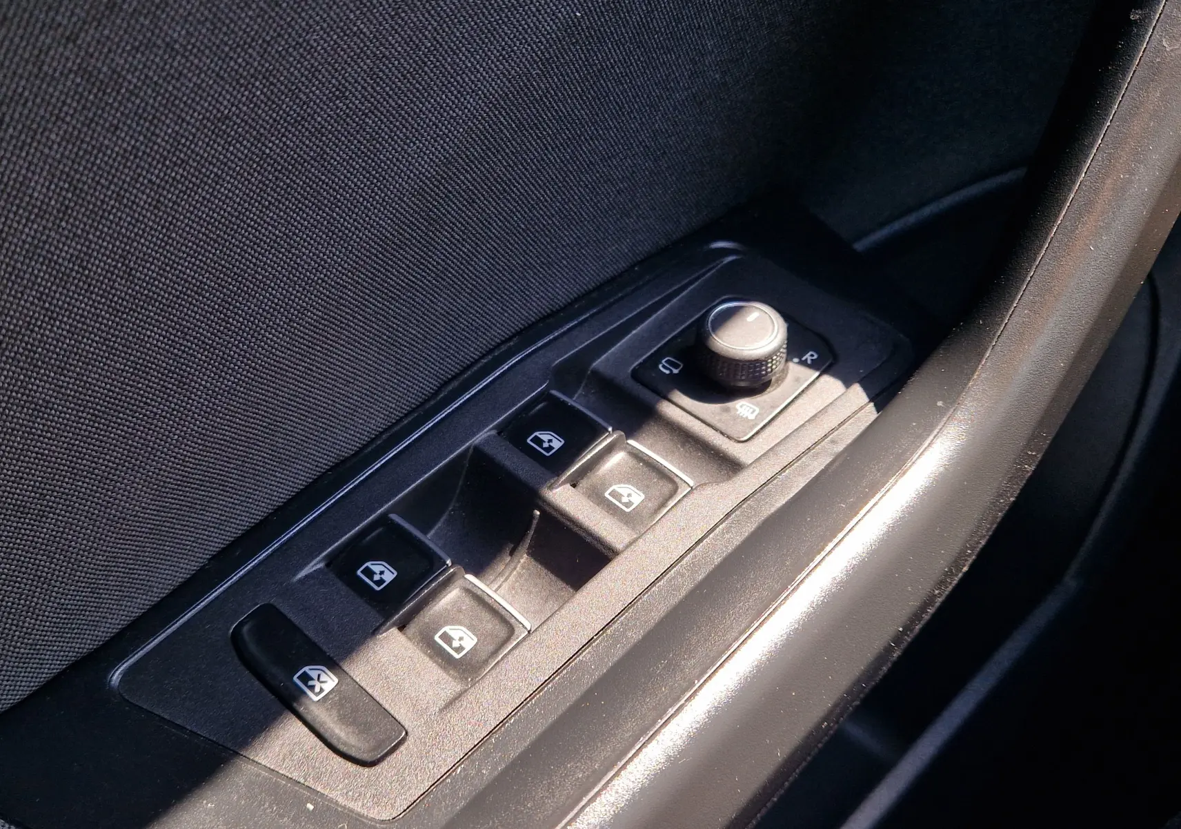 Gros plan sur les commandes des vitres électriques et réglage des rétroviseurs côté conducteur du Volkswagen T-Roc gris foncé.