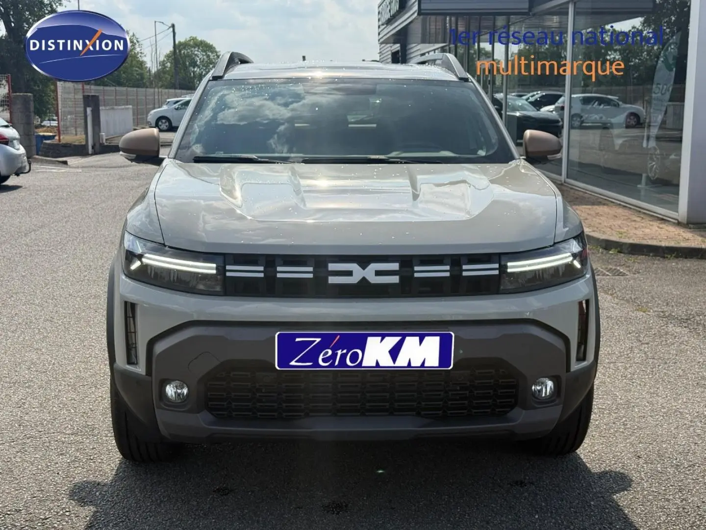 Vue avant d'un Dacia Duster blanc Glacier 2026 avec calandre noire et feux LED allumés sur parking extérieur.
