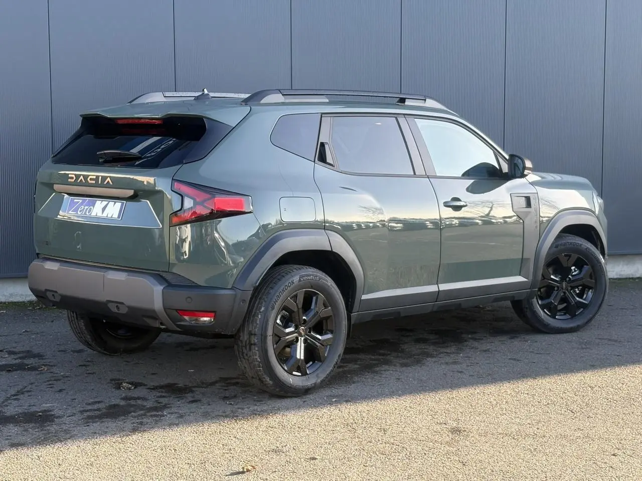 Vue 3/4 arrière droite du Dacia Duster 2026 kaki Lichen avec jantes alliage noires et barres de toit grises.