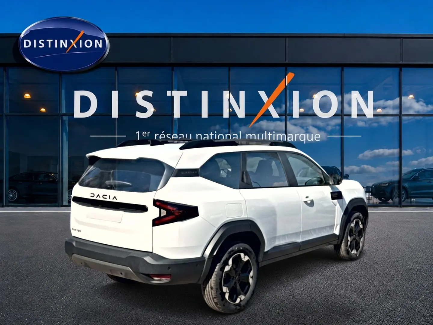 Vue 3/4 arrière droite du SUV blanc Dacia Bigster 2026 avec barres de toit noires et jantes alu distinctives.