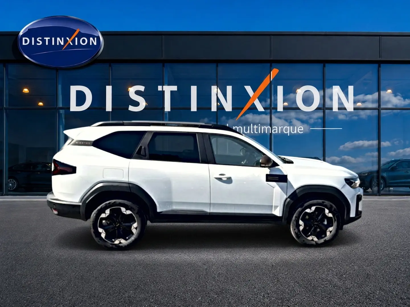 Profil droit du Dacia Bigster blanc 2026 avec jantes noires et toit contrasté devant une vitrine Distinxion multimarque.