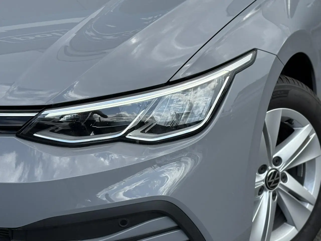 Gros plan sur l'avant droit de la Volkswagen Golf VIII gris lunaire, mettant en valeur son phare LED et sa jante alliage 16 pouces.
