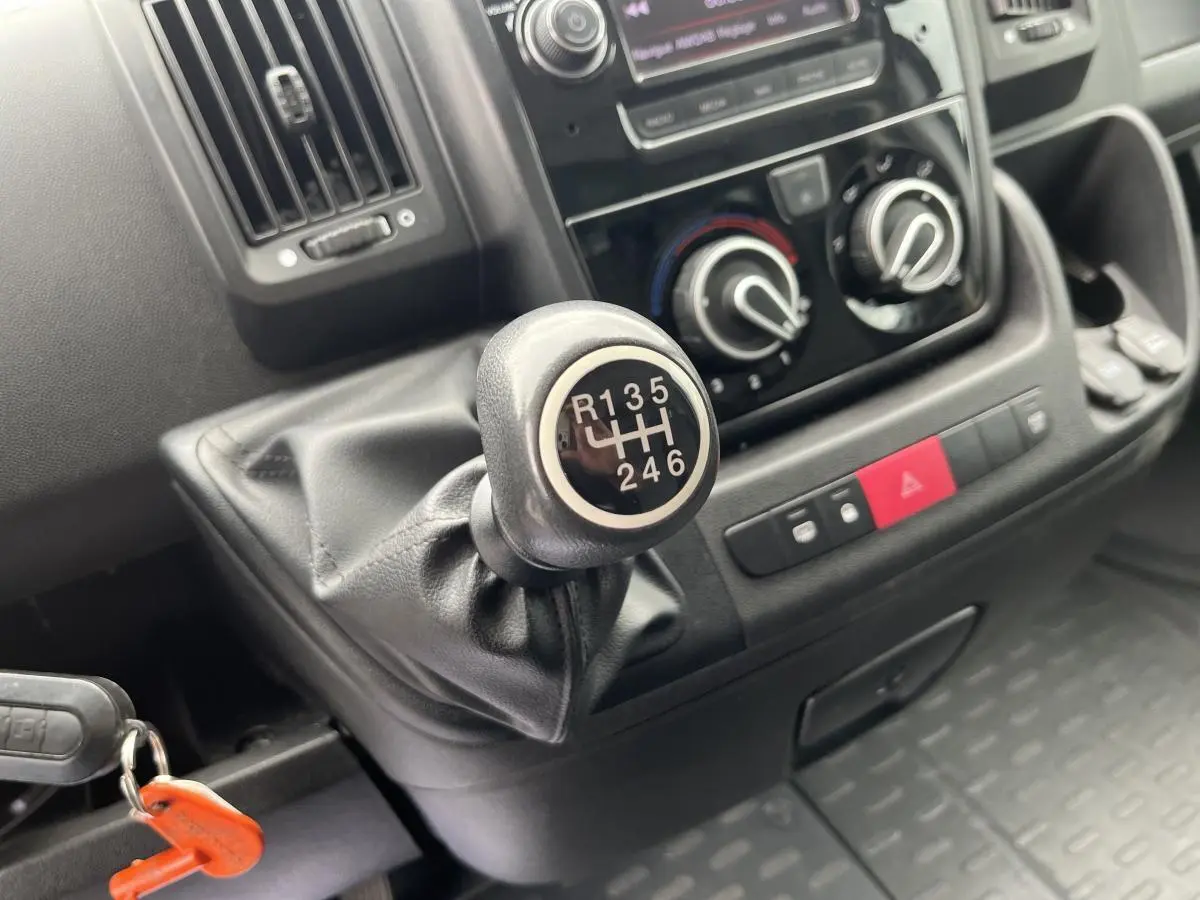 Gros plan sur le levier de vitesses manuel du Fiat Ducato Fourgon blanc, avec tableau de bord et commandes climatisation visibles.