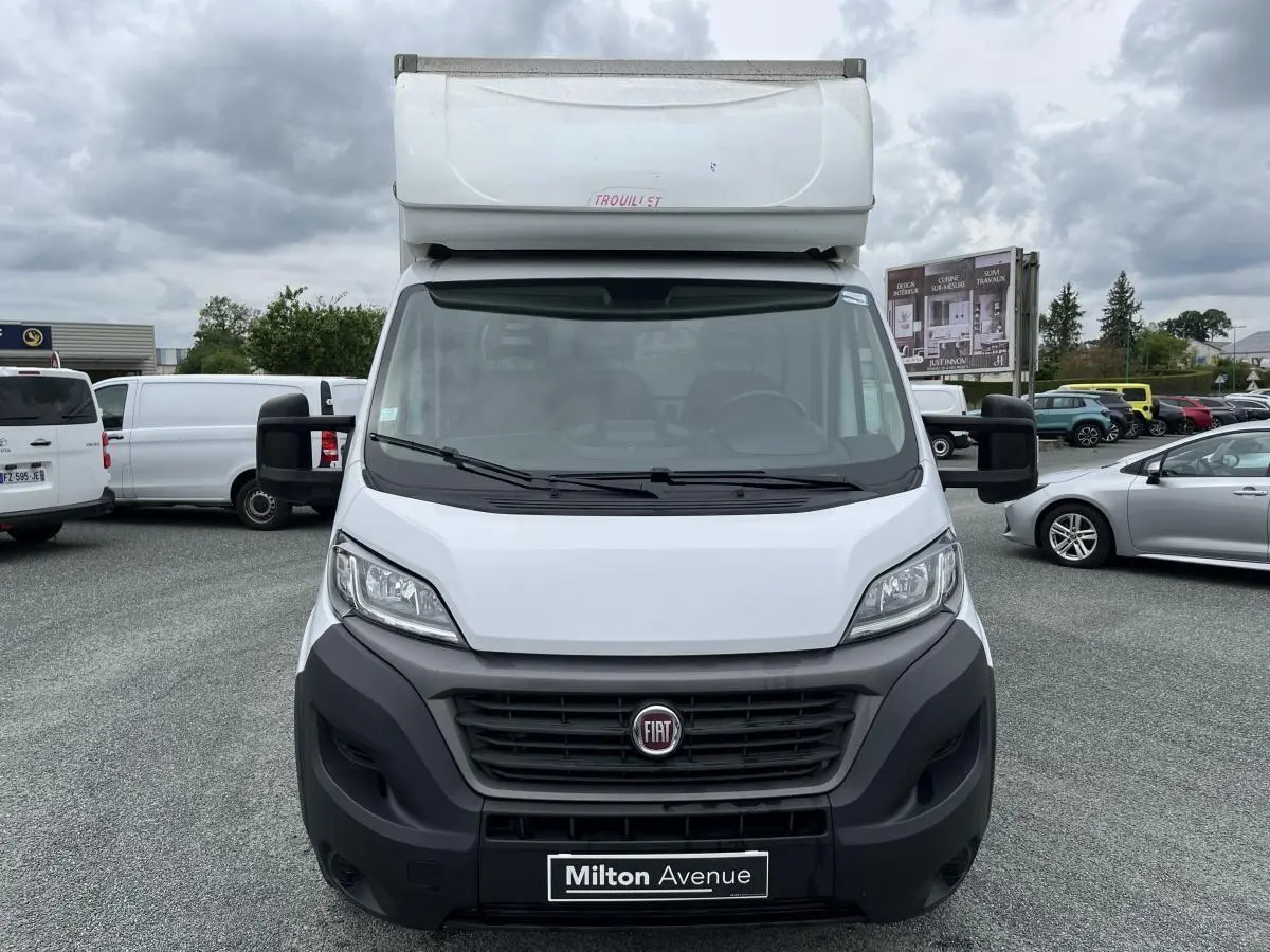 Vue frontale d'un FIAT Ducato Fourgon Maxi Business blanc avec capucine et pare-chocs noirs sur parking.