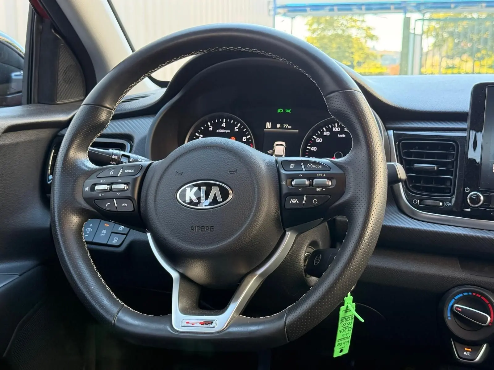 Vue intérieure centrée sur le volant en cuir de la KIA Rio rouge grenadine, avec commandes multifonctions et tableau de bord numérique.