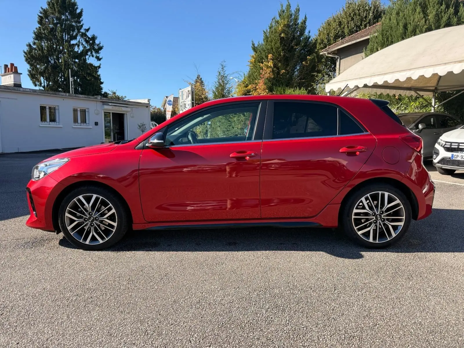 Profil côté gauche d'une KIA RIO rouge grenadine 2022 en finition GT-LINE, avec jantes alliage et lignes dynamiques.