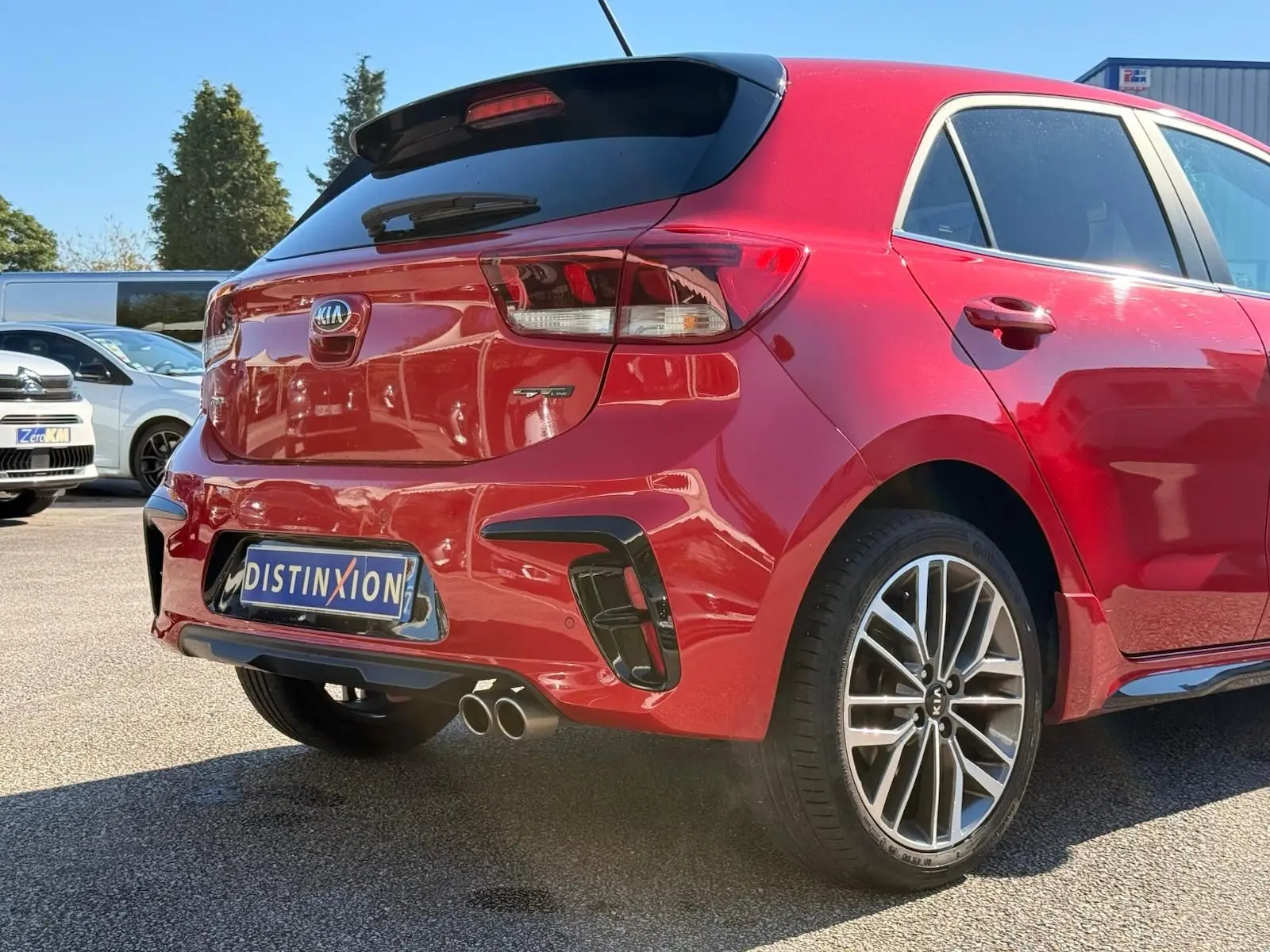 Vue 3/4 arrière droite d'une KIA Rio rouge grenadine 2022 avec double sortie d'échappement et jantes alliage.