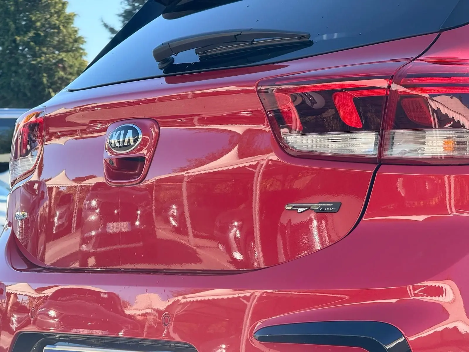 Vue arrière droite d'une KIA RIO rouge grenadine GT-Line 2022 avec logo et feux arrière distinctifs.