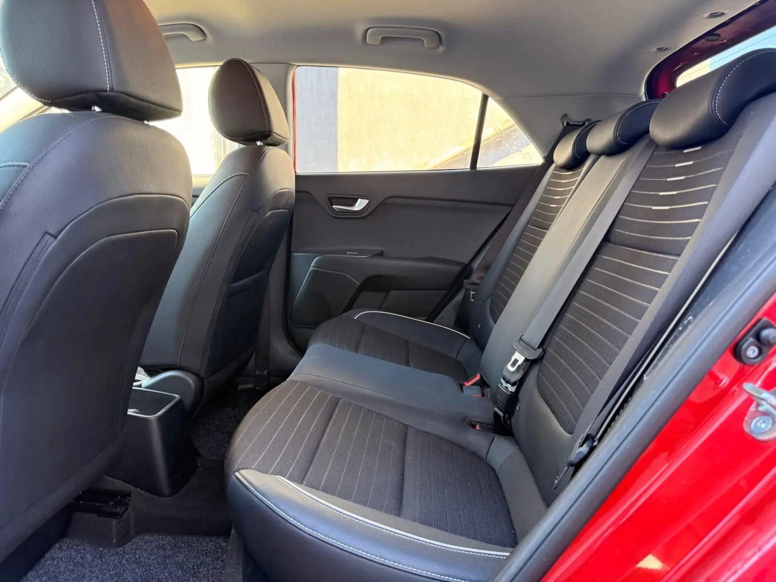 Vue intérieure côté gauche des sièges arrière noirs avec surpiqûres blanches d'une KIA RIO rouge grenadine 2022.