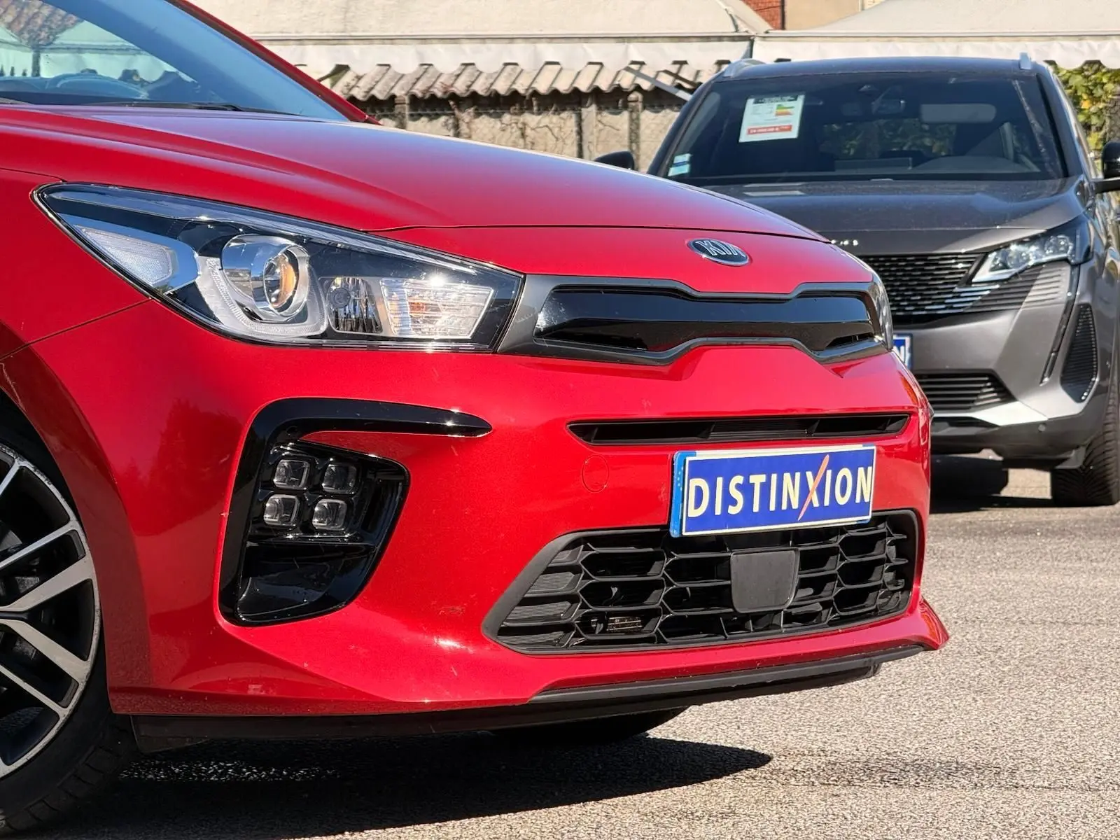 Vue de face en léger 3/4 avant gauche d'une KIA RIO rouge grenadine avec calandre noire et plaque Distinxion.