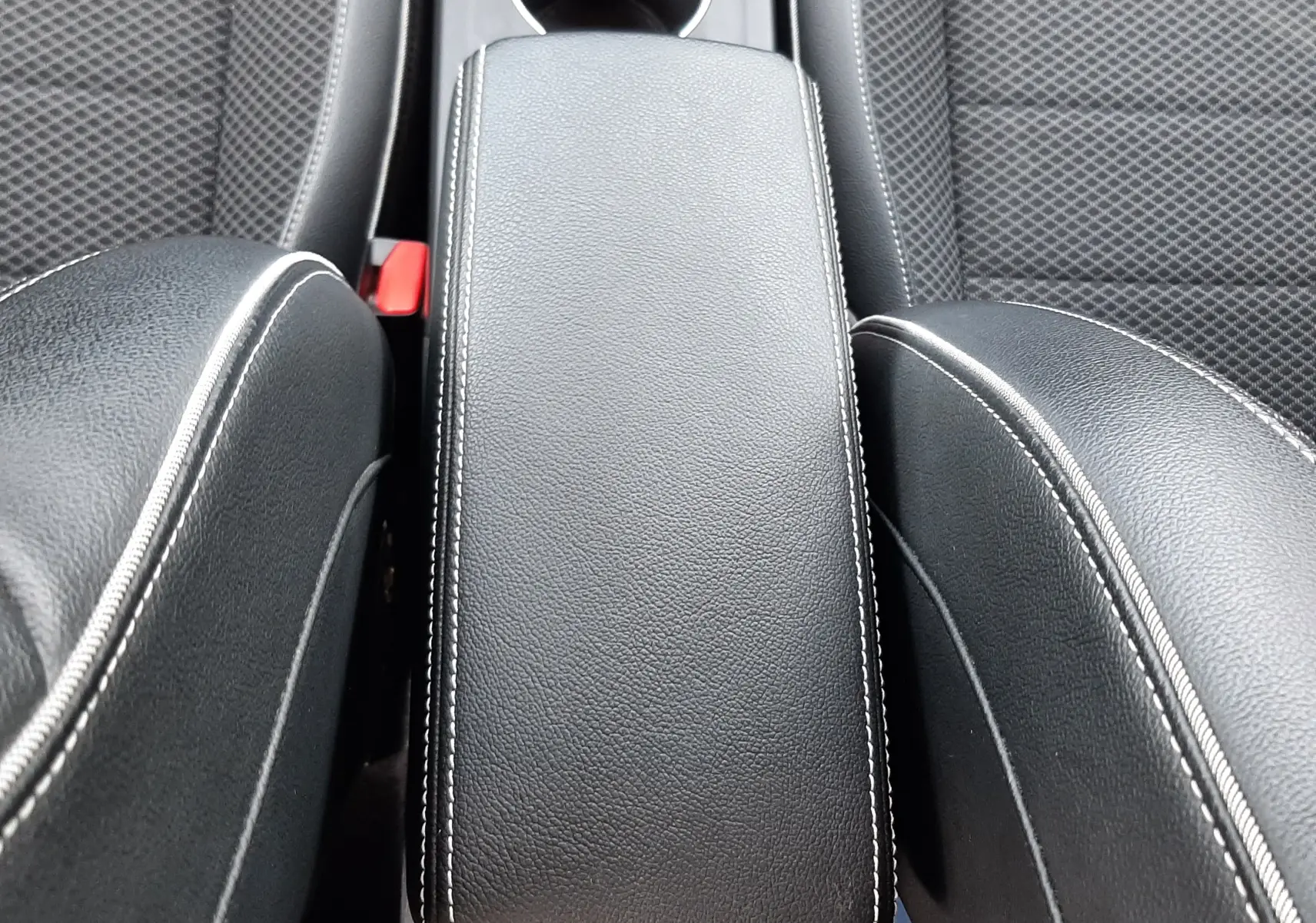 Vue rapprochée de l'accoudoir central noir avec surpiqûres blanches entre deux sièges en tissu gris foncé du Renault Arkana.