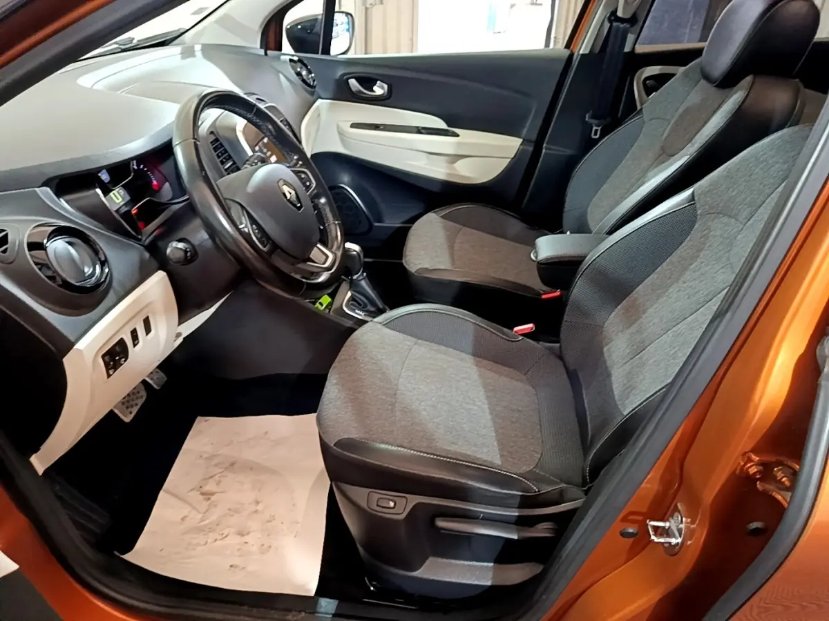 Intérieur avant droit du Renault Captur orange 2019, montrant sièges gris, volant cuir et tableau de bord clair.