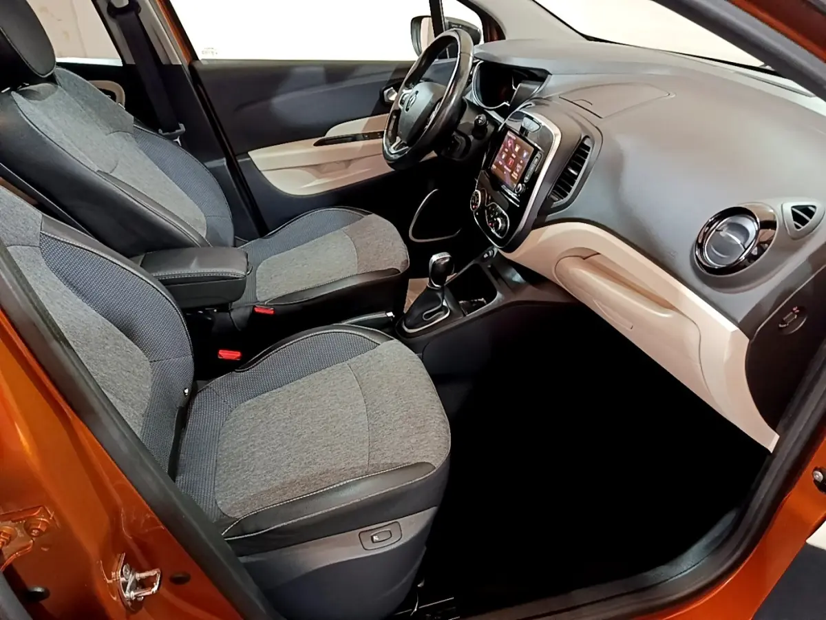 Intérieur avant droit du Renault Captur orange 2019, montrant sièges gris et tableau de bord avec écran tactile.