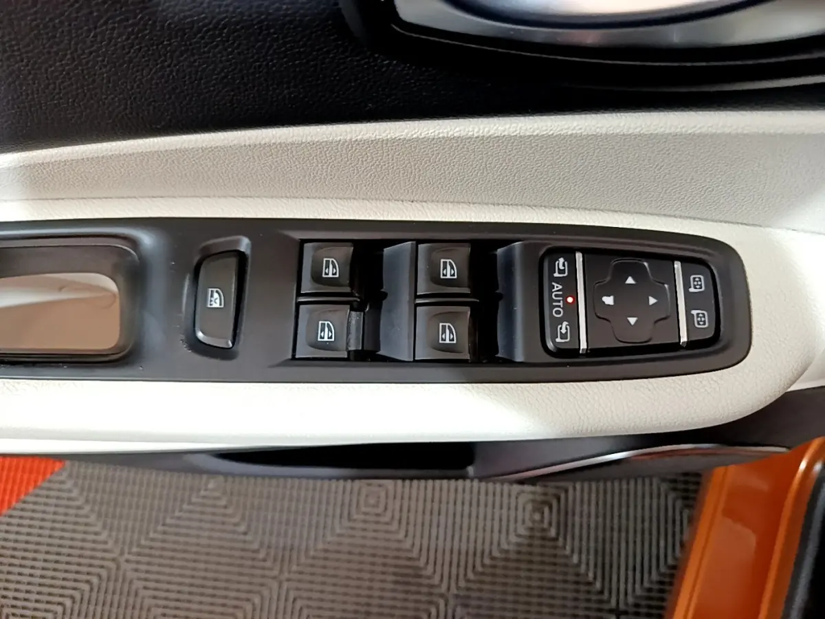 Vue rapprochée des commandes de lève-vitres et réglages des rétroviseurs sur la porte côté gauche du Renault Captur orange.