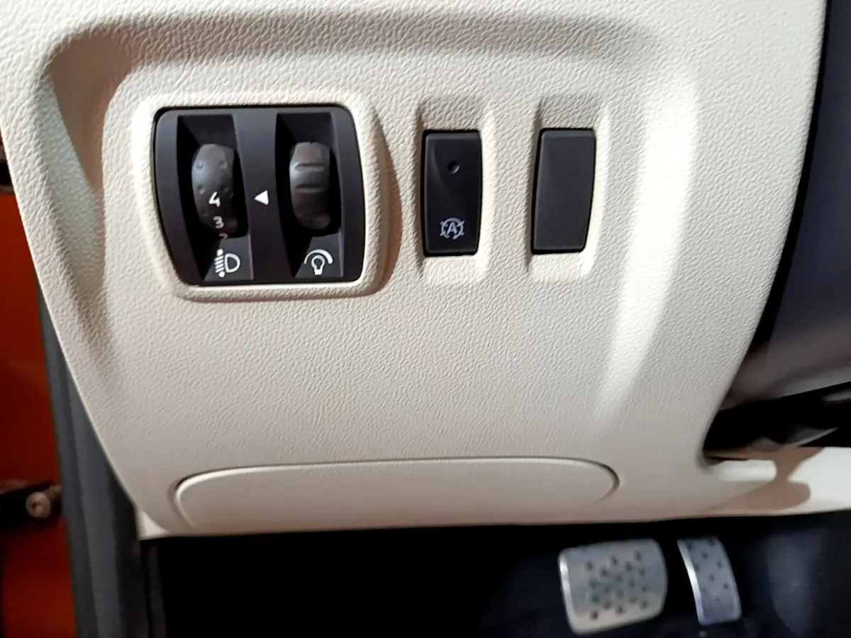 Vue rapprochée des commandes de réglage des phares et du tableau de bord beige du Renault Captur Intens orange 2019.